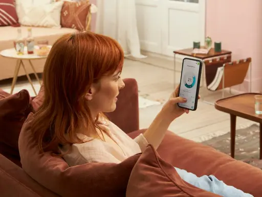 Donna con capelli rossi controlla app Daikin sul telefono, mostrando la differenza tra Daikin e Daikin Siesta per il comfort domestico.