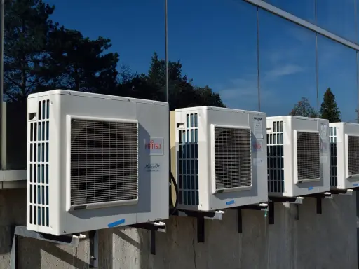 Unità esterne di condizionatori Fujitsu, montate su staffe, riflettono alberi e cielo. Il loro funzionamento è silenzioso, con un basso livello sonoro.