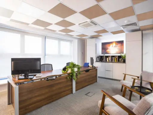 Ufficio moderno con scrivania in legno, computer e due poltrone. Il controsoffitto antirumore a scacchiera bianca e marrone migliora l'acustica.