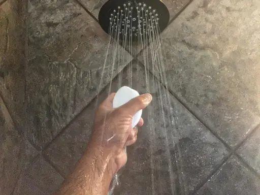 Mano che tiene una saponetta sotto la doccia, con getti d'acqua che suggeriscono il desiderio di aumentare pressione acqua doccia.
