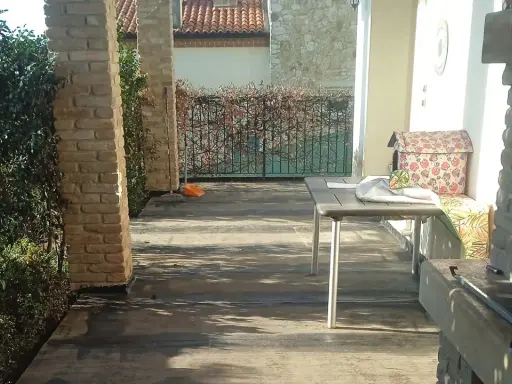 Terrazzo con pavimentazione scura, ideale per l'impermeabilizzazione. Tavolo, barbecue e vegetazione completano la scena.