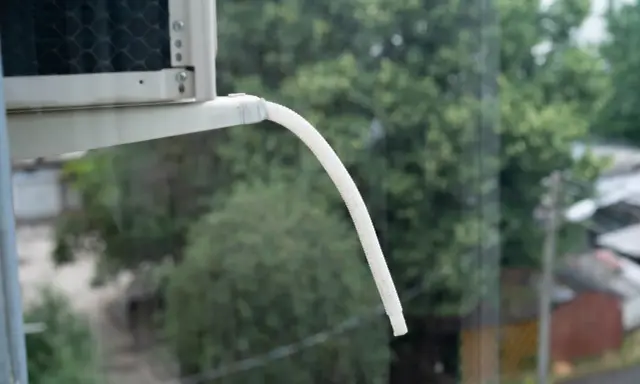 Tubo bianco flessibile per lo scarico condensa condizionatore, sporge da un'unità esterna, con alberi verdi sullo sfondo.
