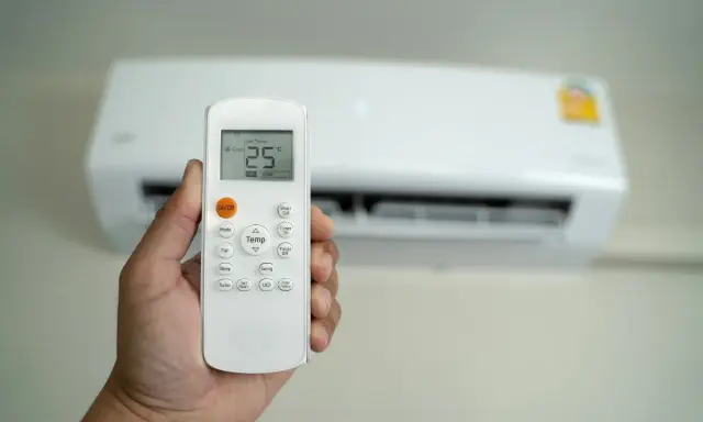 Mano che tiene un telecomando per condizionatore, impostato a 25°C. Il significato di "set temp condizionatore" è la temperatura desiderata.