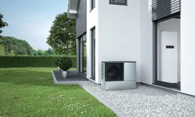 Unità esterna per riscaldamento con condizionatore, posizionata accanto a una casa moderna con giardino curato.
