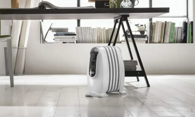 Un radiatore ad olio bianco, sotto una scrivania, mostra come funziona per riscaldare l'ambiente.