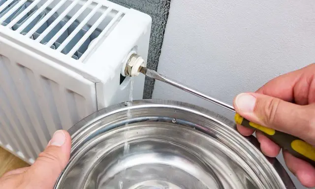 Si sta svuotando un termosifone per capire come è fatto all'interno. L'acqua esce da una valvola e cade in una bacinella.
