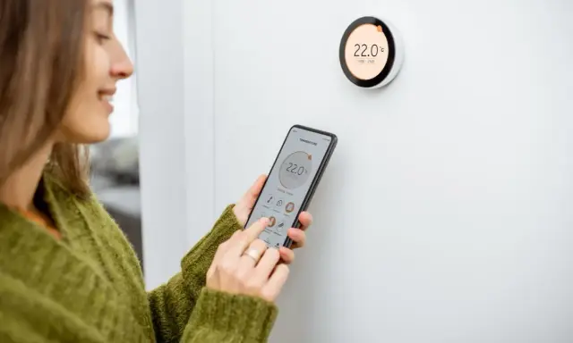 Donna controlla il termostato del riscaldamento tramite smartphone, mostrando come funziona il controllo intelligente della temperatura domestica.