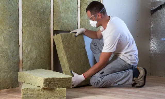 Operaio con maschera e occhiali installa pannelli di lana di roccia per cappotto interno, prima del cartongesso.