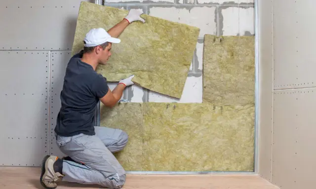 Operaio posiziona pannelli isolanti per il cappotto casa. L'isolamento termico è fondamentale per il comfort abitativo.