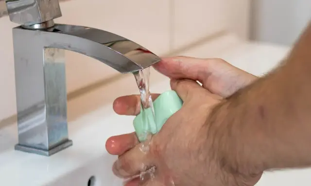 Mani che si lavano sotto un rubinetto cromato, con un getto d'acqua che indica una buona pressione dell'acqua dell'acquedotto.