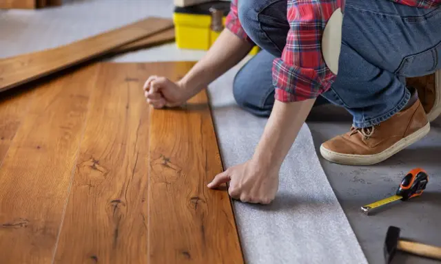 Persona posiziona assi di legno su un tappetino isolante, un passo fondamentale per come insonorizzare il pavimento e ridurre i rumori.