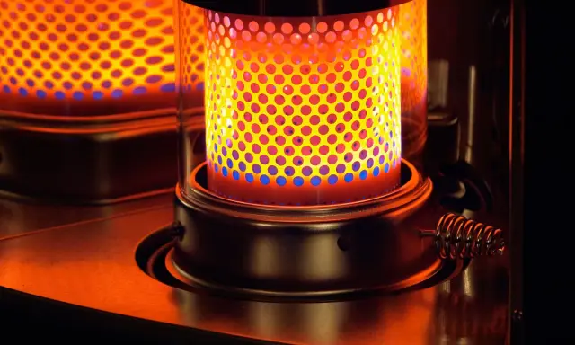 La stufa a kerosene pericolosa emana un calore intenso, con fiamme blu e gialle che danzano attraverso la griglia forata.