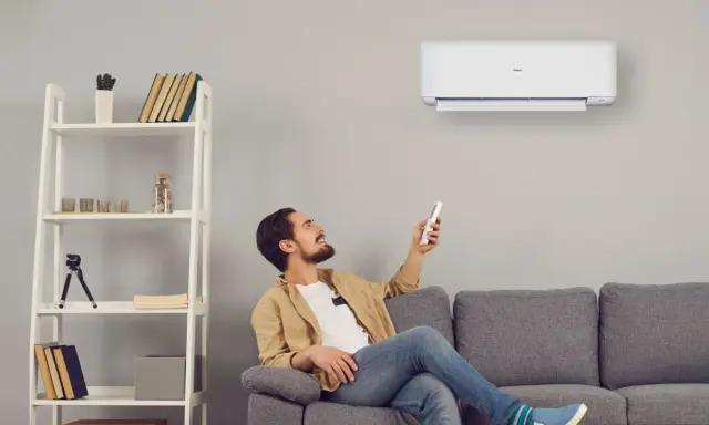 Uomo sorride usando telecomando per accendere un cool condizionatore. Il suo significato è comfort e benessere in casa.