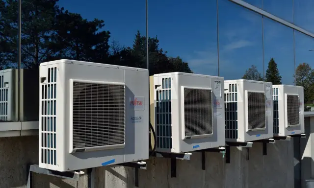 Unità esterne di condizionatori Fujitsu, montate su staffe, riflettono alberi e cielo. Il loro funzionamento è silenzioso, con un basso livello sonoro.