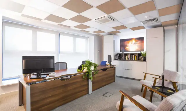 Ufficio moderno con scrivania in legno, computer e due poltrone. Il controsoffitto antirumore a scacchiera bianca e marrone migliora l'acustica.