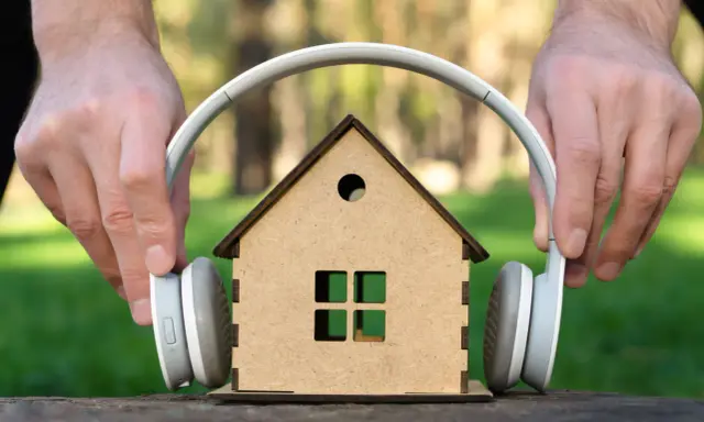Mani posizionano cuffie su una casa giocattolo, come se volessero ascoltare suoni a 110 decibel.