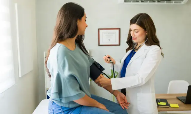 Medico con stetoscopio misura la pressione a una paziente, mostrando come misurare la pressione manualmente.
