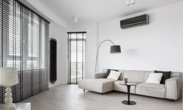 Unità interna di climatizzatore su parete bianca, con divano e lampada. Ideale per capire la differenza tra monosplit e dualsplit.