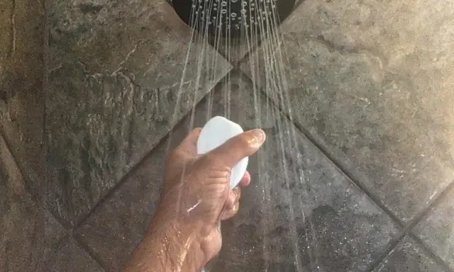 Mano che tiene una saponetta sotto la doccia, con getti d'acqua che suggeriscono il desiderio di aumentare pressione acqua doccia.