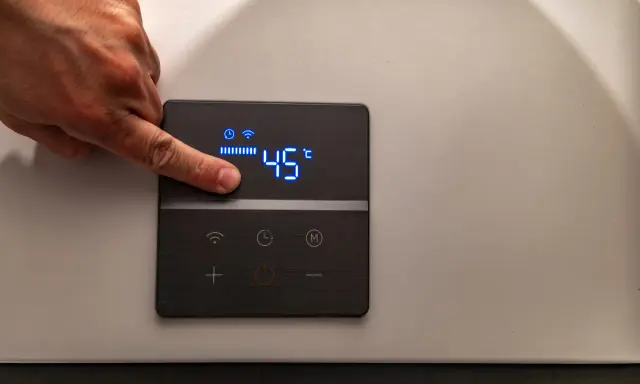 Dito un dito regola la temperatura su una caldaia elettrica a condensazione, impostata a 45°C.