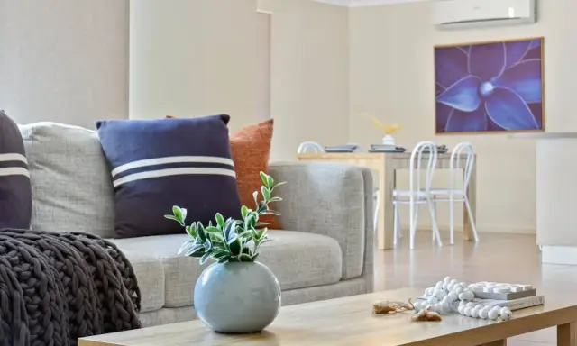 Soggiorno moderno con divano grigio, cuscini decorativi e un condizionatore per rendere smart l'ambiente. Tavolo da pranzo e quadro floreale sullo sfondo.