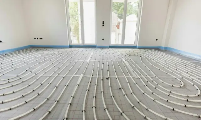 Installazione di riscaldamento a pavimento. Tubi bianchi disposti a serpentina su un foglio isolante, pronti per la posa del massetto. La temperatura dell'acqua sarà regolata per un comfort ottimale.