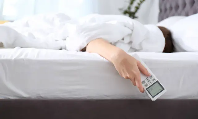Mano che tiene il telecomando del condizionatore, con la persona che cerca il **significato** di un **sonno** confortevole.