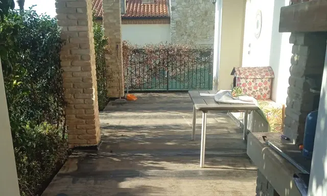 Terrazzo con pavimentazione scura, ideale per l'impermeabilizzazione. Tavolo, barbecue e vegetazione completano la scena.