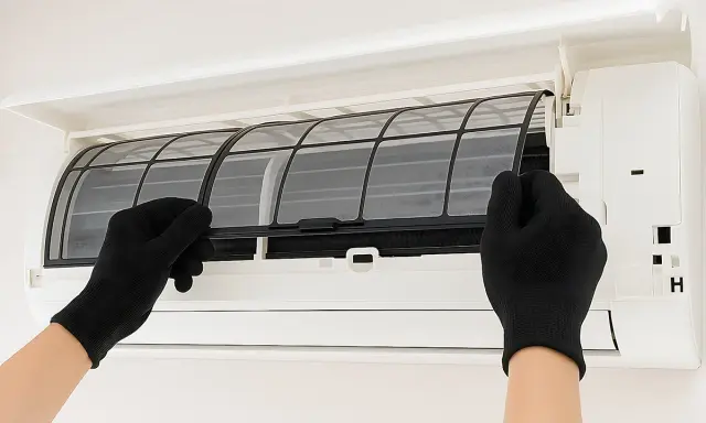 Mani con guanti neri estraggono i filtri da un condizionatore, mostrando come pulire i filtri del condizionatore per un'aria più fresca.