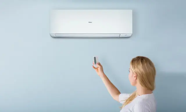 Donna usa il telecomando per regolare il condizionatore Haier. Il significato di "heat condizionatore" è la sua capacità di riscaldare.