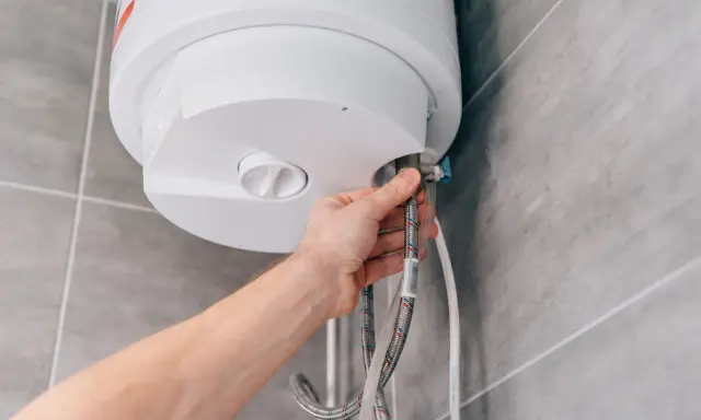 Mano che collega un tubo a uno scaldabagno a gas. La domanda è: quanto dura uno scaldabagno a gas?