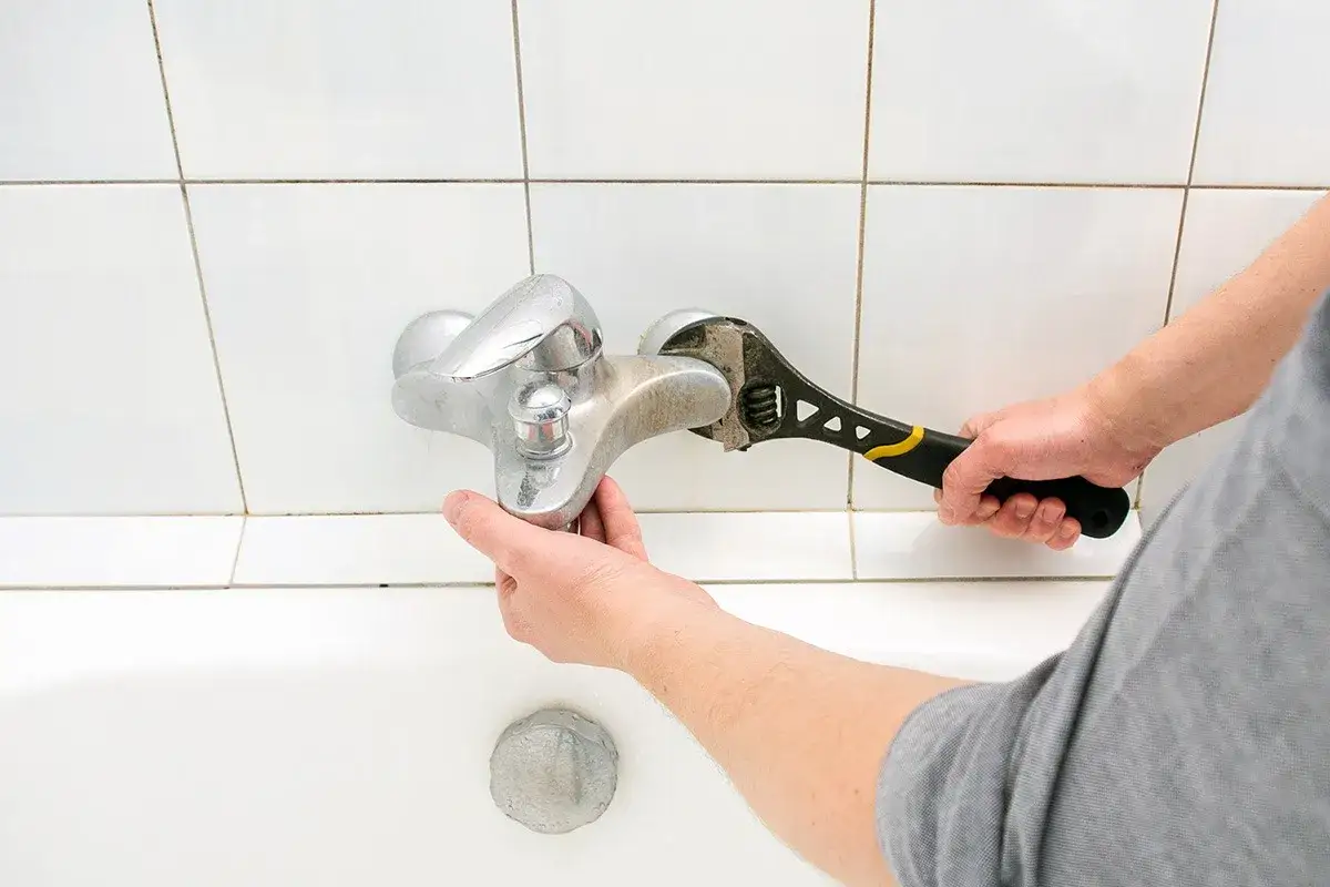 Mano con chiave inglese ripara un rubinetto che gocciola sopra la vasca da bagno.