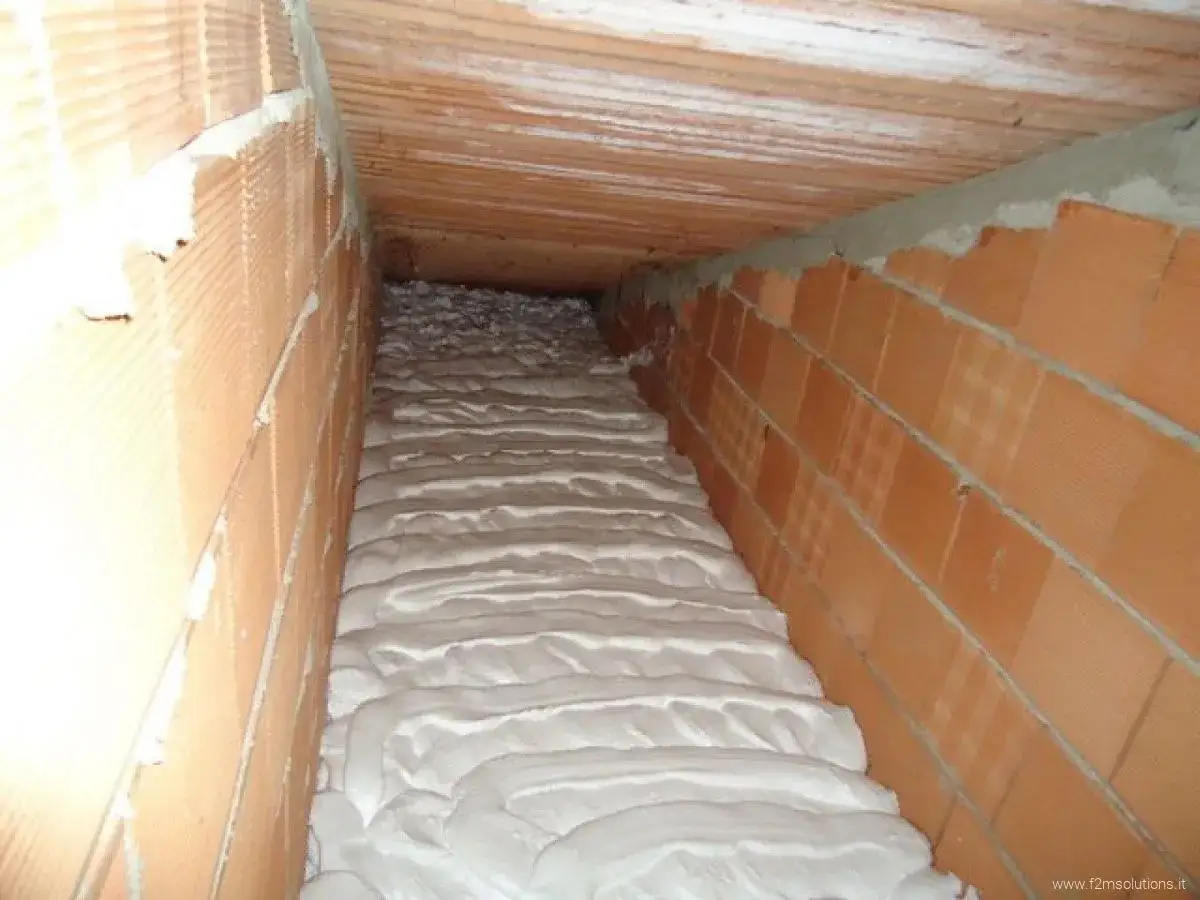 Schiuma isolante termica applicata in un sottotetto, tra pareti di mattoni forati e tetto in legno.