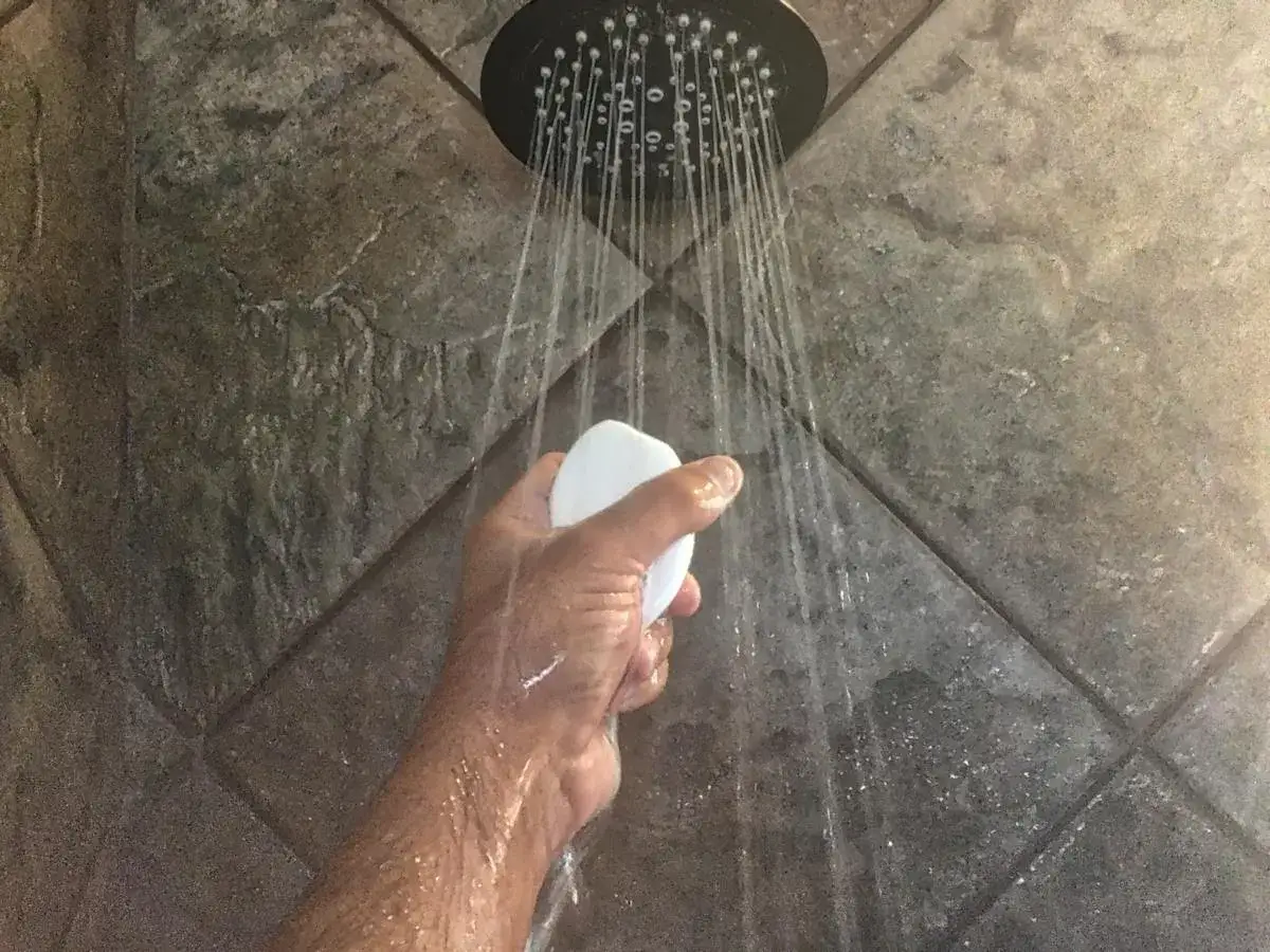 Mano che tiene una saponetta sotto la doccia, con getti d'acqua che suggeriscono il desiderio di aumentare pressione acqua doccia.