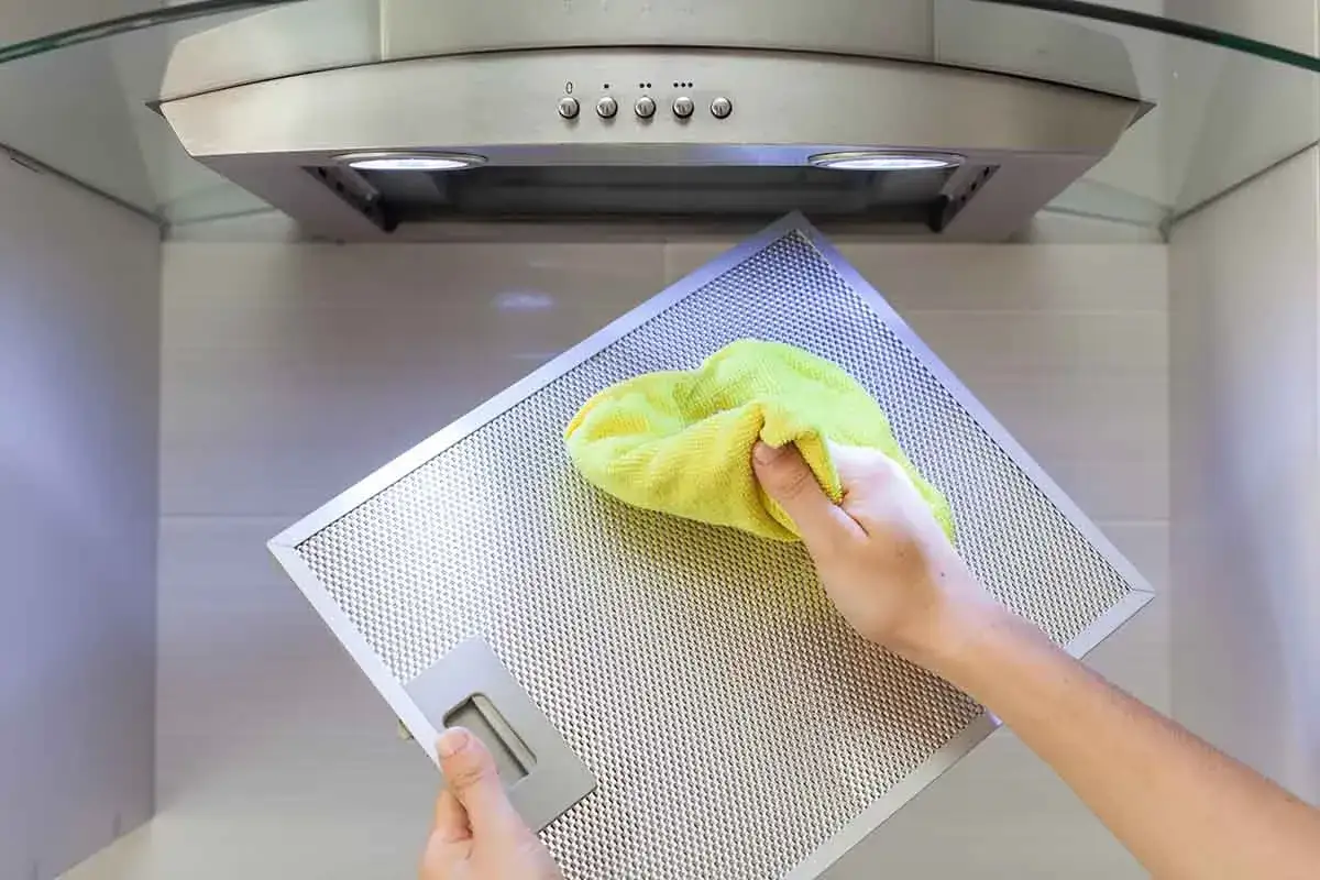 Mano pulisce filtro cappa con panno giallo. Impara come pulire i filtri della cappa per una cucina più sana.