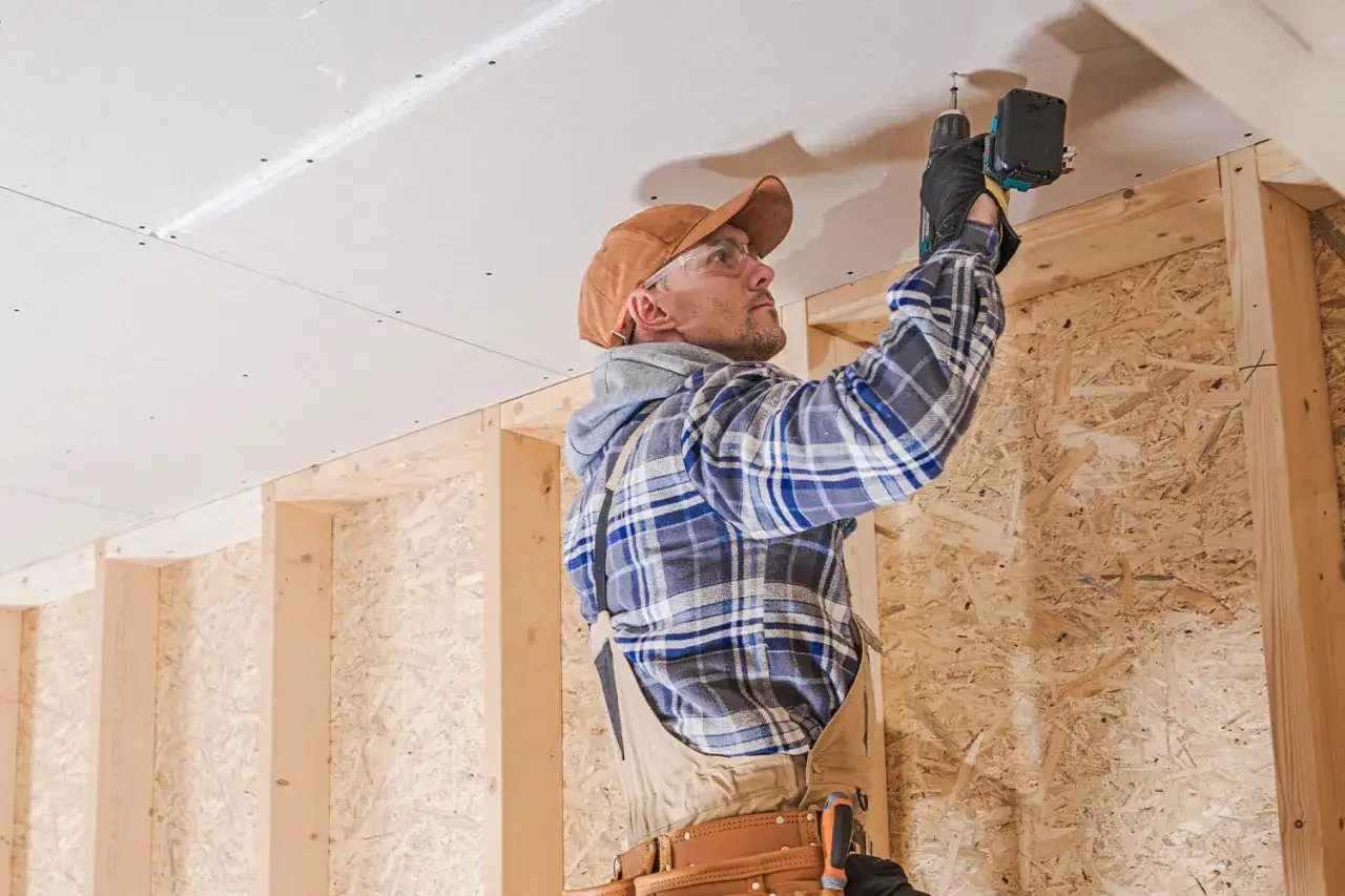 Operaio con trapano avvita cartongesso al soffitto, un passo per come insonorizzare una stanza in modo economico.