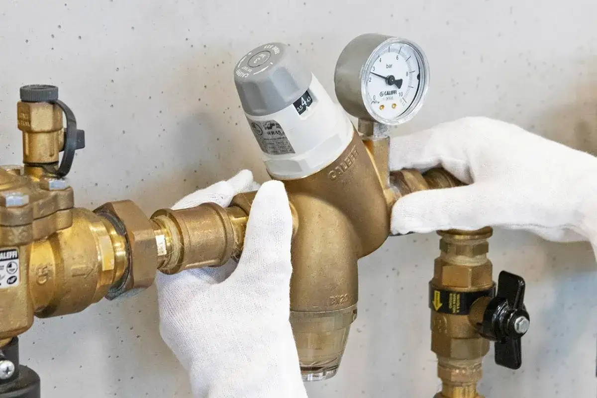 Mani guantate installano un riduttore di pressione acqua, mostrando come funziona con manometro e regolazione.