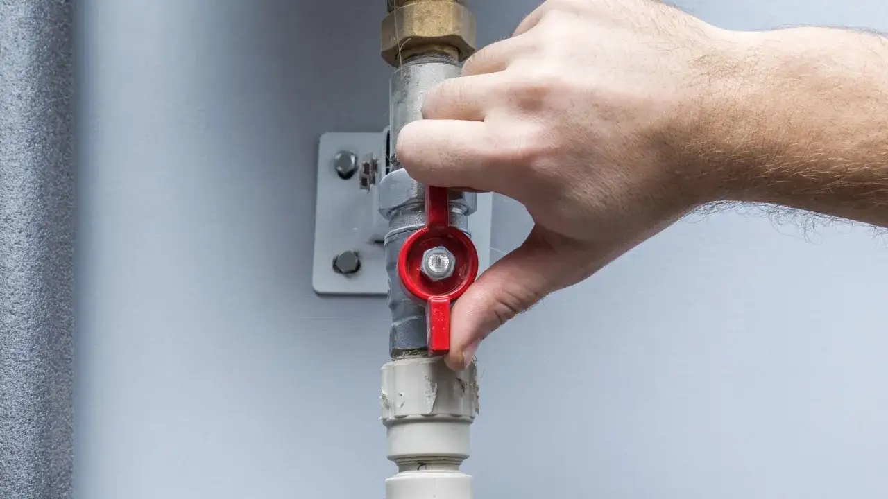 Mano che gira la leva rossa per la chiusura rubinetto acqua senso orario, fermando il flusso.