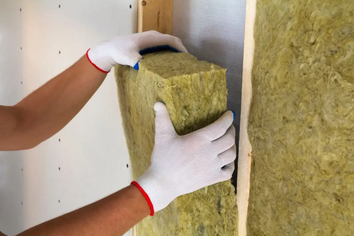 Mani guantate inseriscono isolante in lana di roccia in una parete, creando un cappotto casa efficiente.