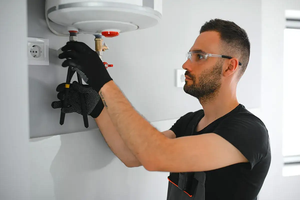 Un tecnico con occhiali protettivi controlla un boiler, forse per capire perché i termosifoni non si scaldano.