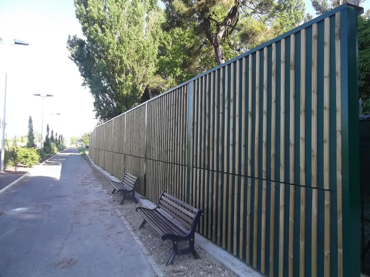 Una lunga barriera antirumore fai da te in legno protegge un sentiero alberato.