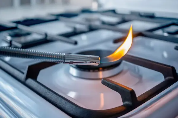 Accensione di un fornello a gas con un accendigas. La fiamma arancione danza, alimentata dal **natural gas**.