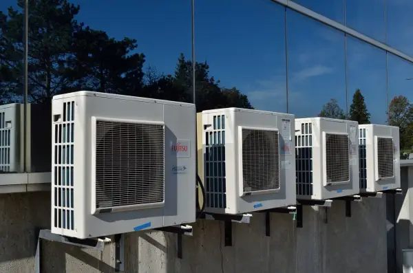 Unità esterne di condizionatori Fujitsu, montate su staffe, riflettono alberi e cielo. Il loro funzionamento è silenzioso, con un basso livello sonoro.