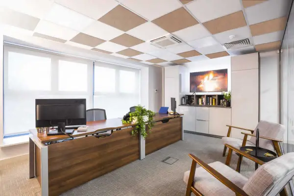 Ufficio moderno con scrivania in legno, computer e due poltrone. Il controsoffitto antirumore a scacchiera bianca e marrone migliora l'acustica.