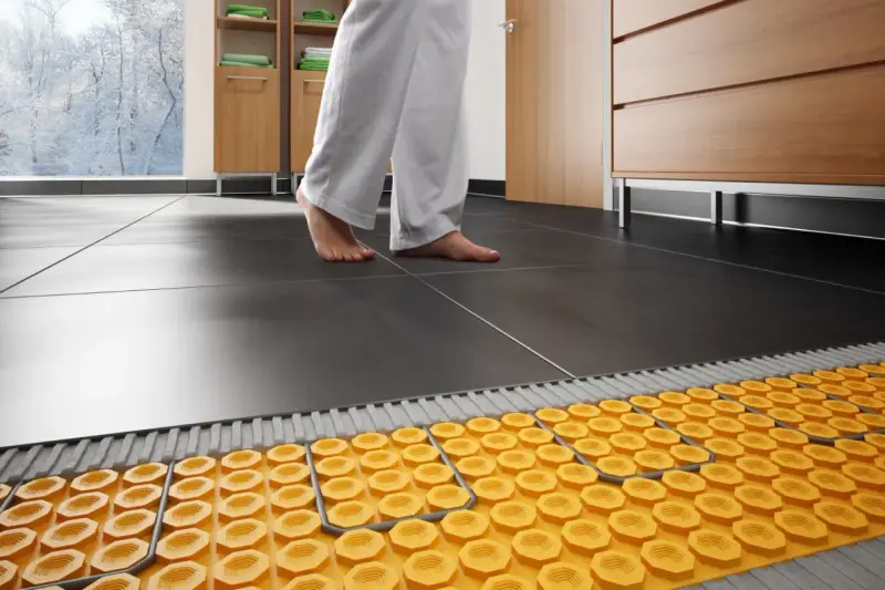 Piedi nudi su piastrelle scure, con un sistema di riscaldamento a pavimento visibile sotto. Addio termosifoni, benvenuta comodità!